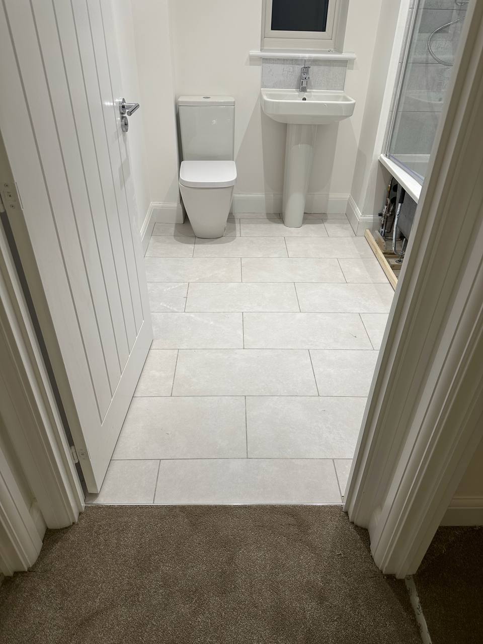 Light tile-effect bathroom floor with carpet at the threshold